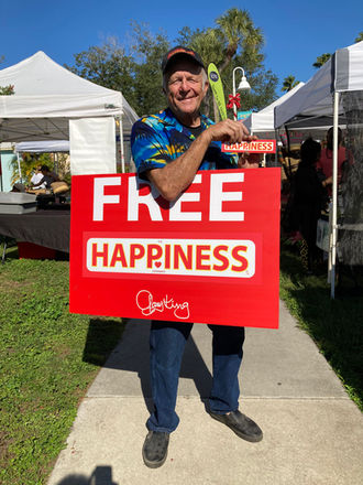 Gary King at an outdoor market with a FREE HAPPINESS sign
