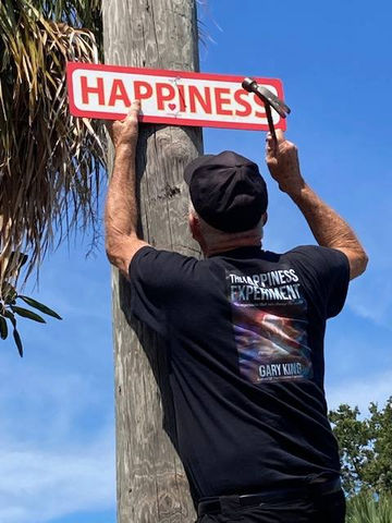 Gary King nailing a HAPPINESS sign to a utility pole